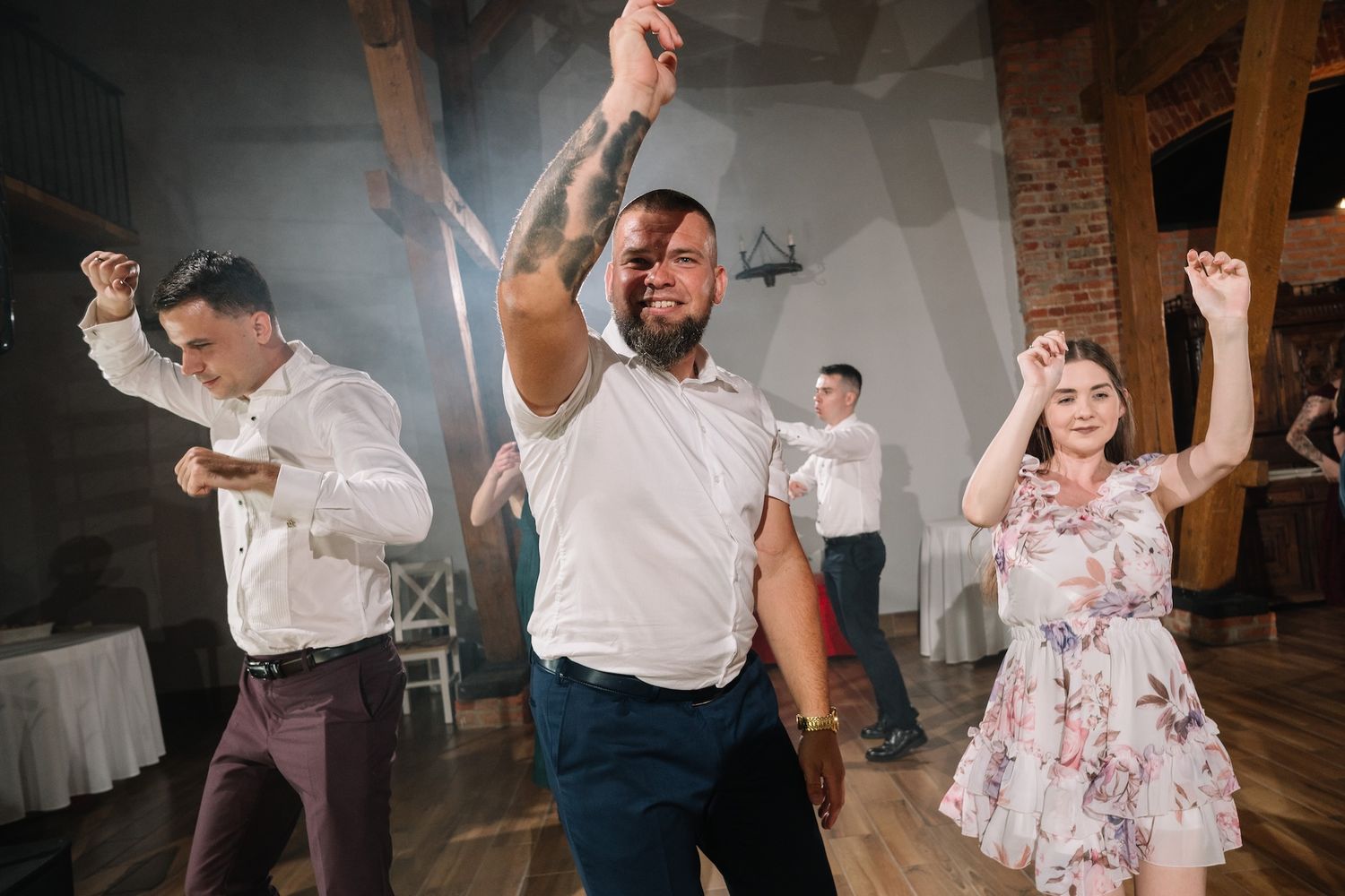 Guests dancing enthusiastically with arms raised at a lively indoor wedding reception celebration.