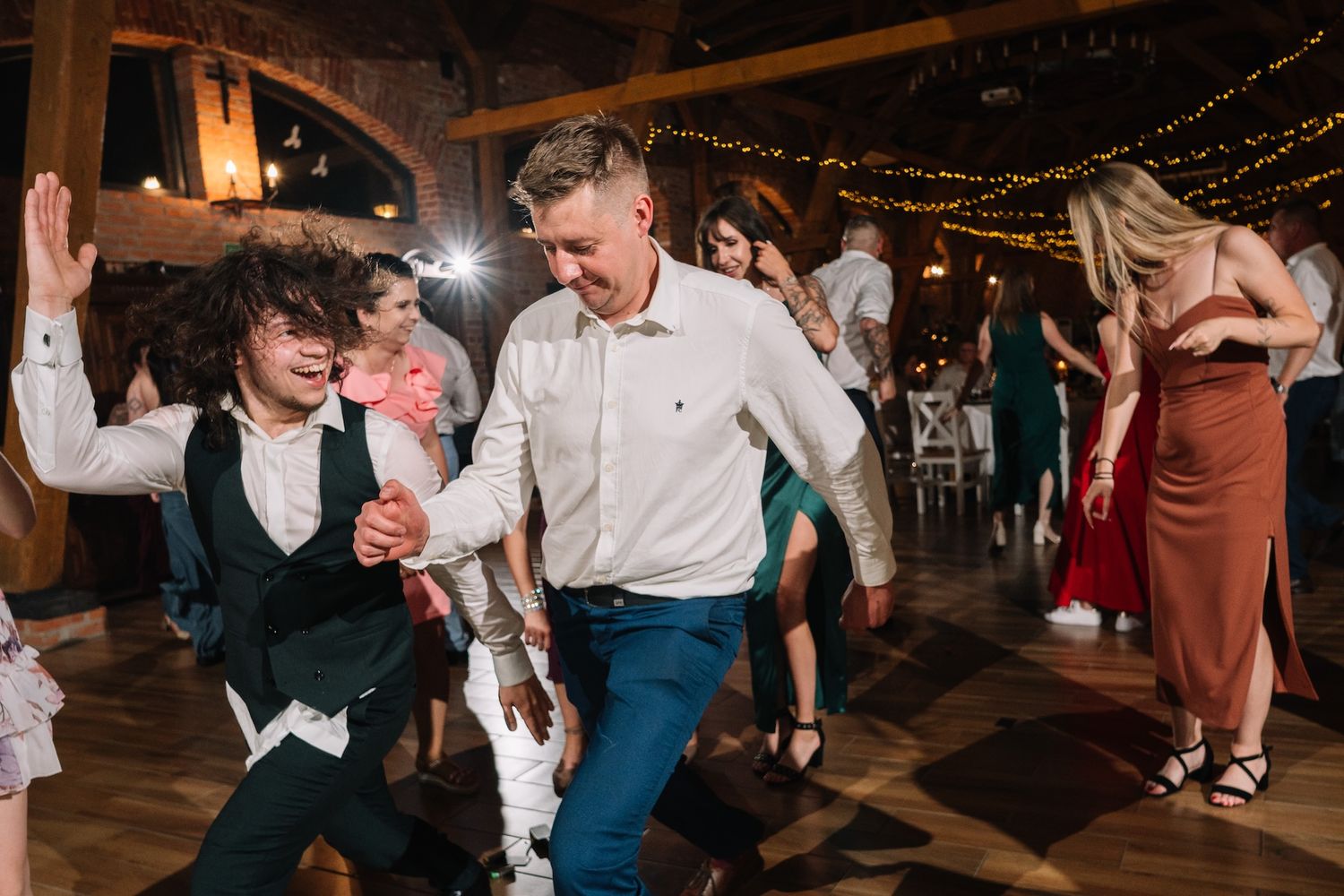 Man and curly-haired child dancing together joyfully at a festive wedding reception party.