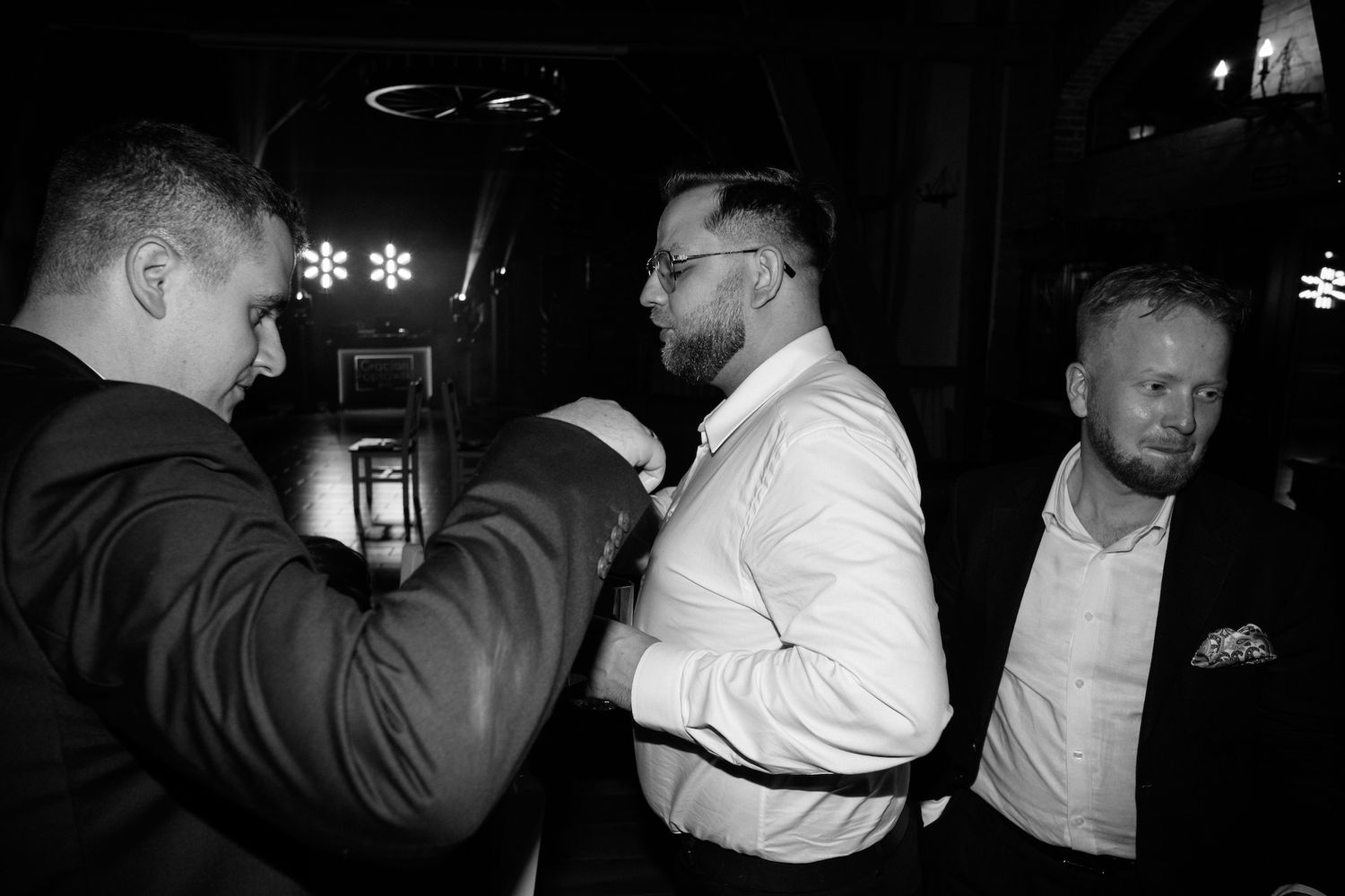 Black and white photo of three men in formal attire gathered together at a wedding event.