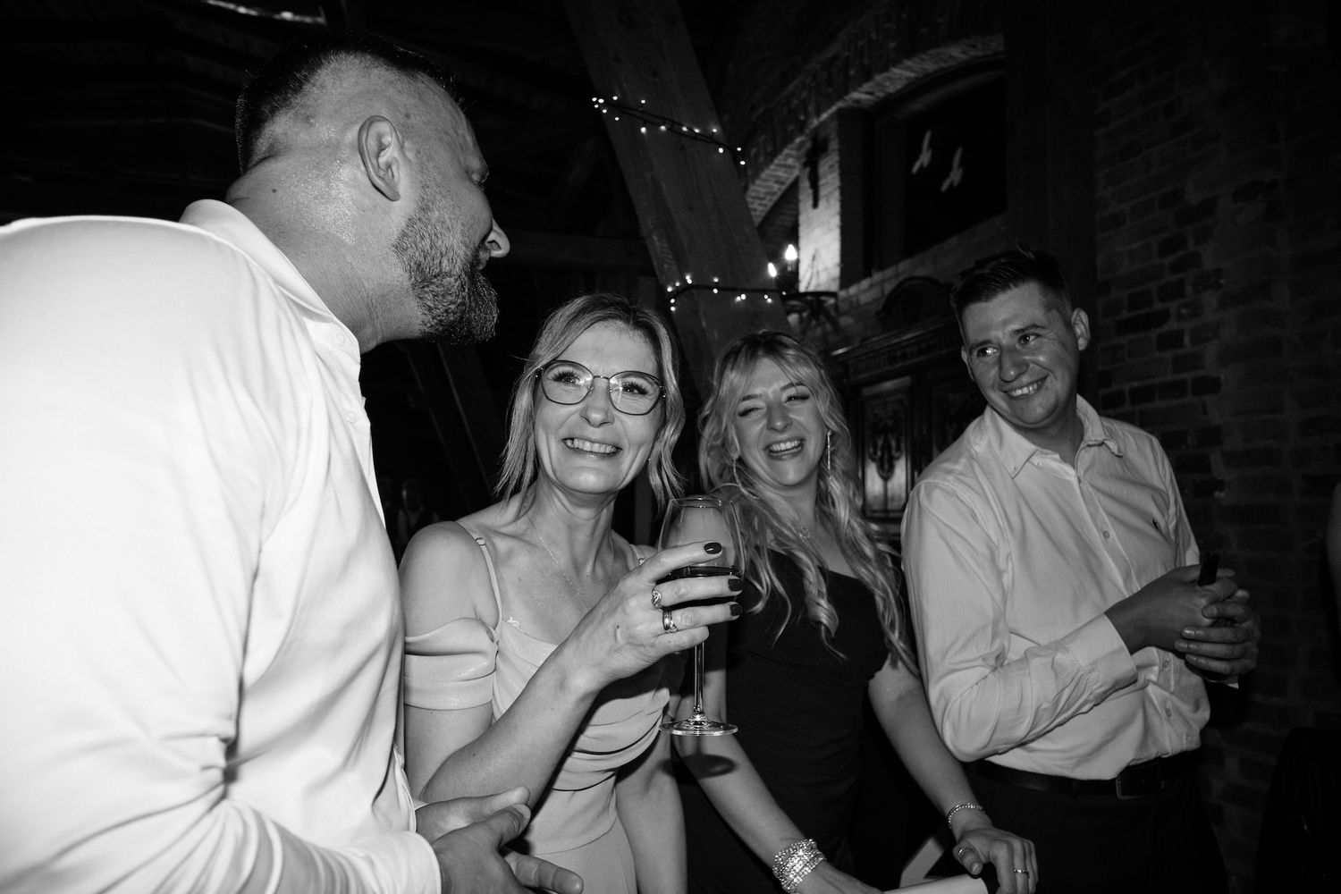 Black and white photo of four smiling wedding guests socializing and enjoying drinks at reception.