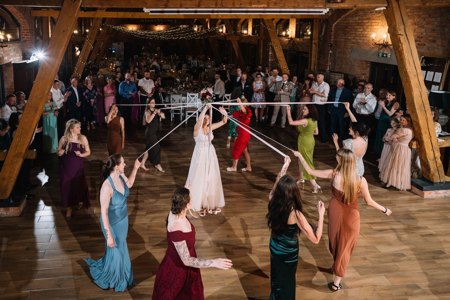 Aerial view of bride and guests playing ribbon bouquet toss game on dance floor at wedding reception.