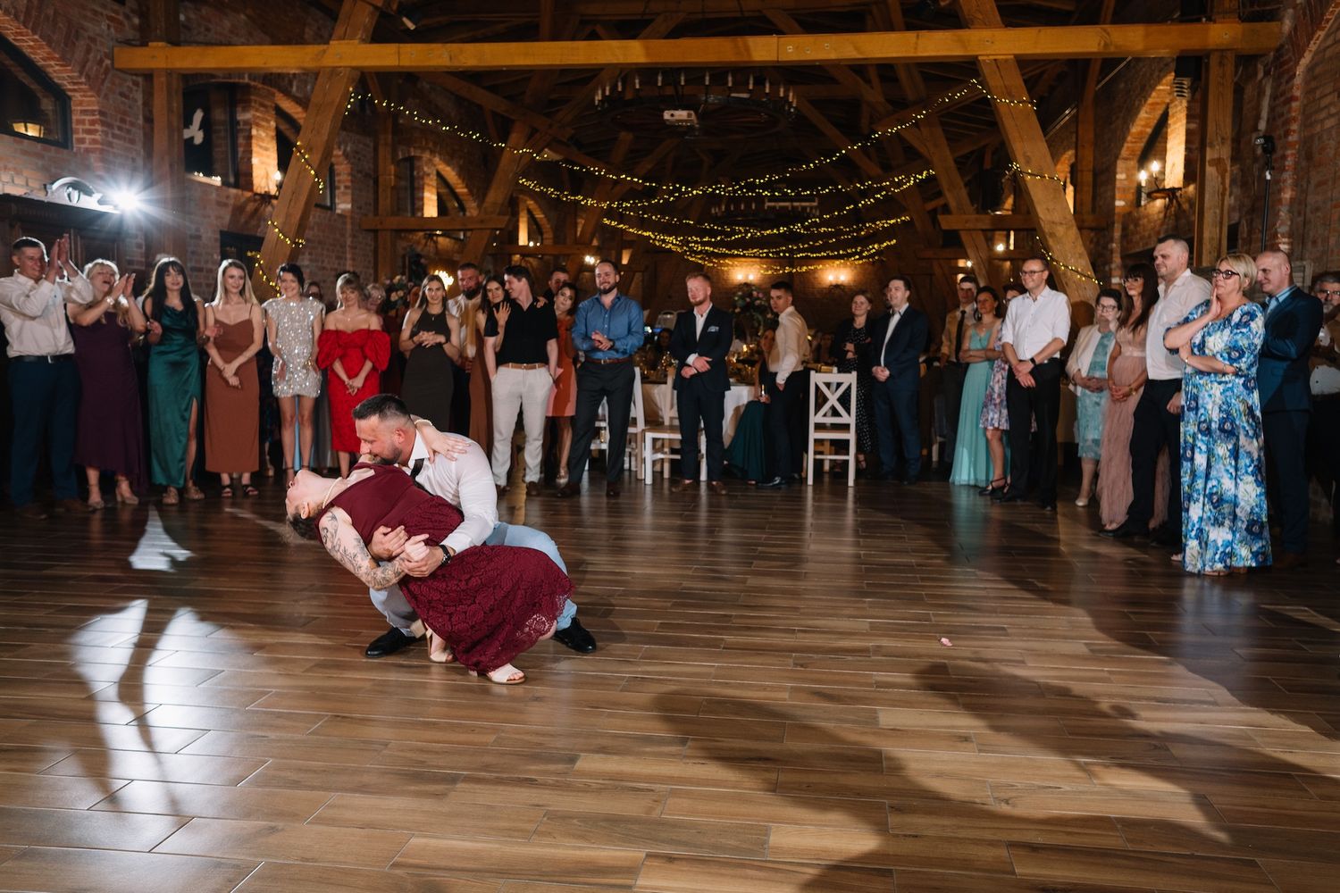 Couple shares dramatic dip dance move on wooden floor at rustic barn wedding reception.