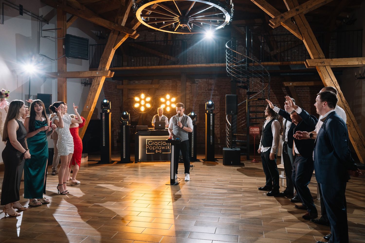 Wedding MC addresses guests holding microphone on dance floor of rustic barn reception venue.