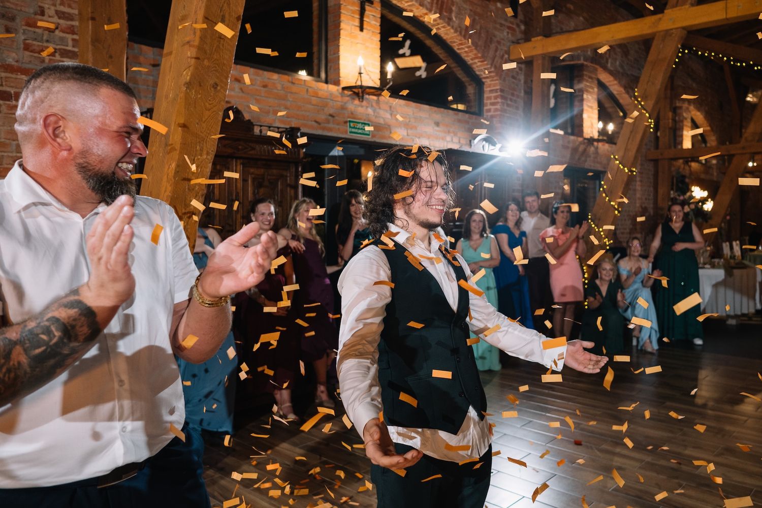 Bride and groom celebrating with golden confetti shower at elegant barn wedding reception with guests.