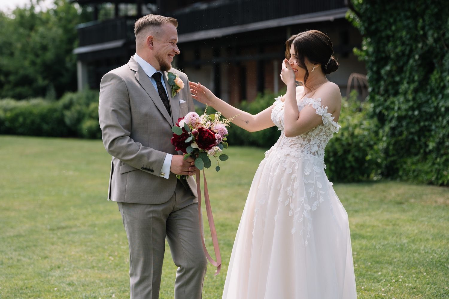 Emotional bride wipes tears as groom holds bridal bouquet during outdoor first look.