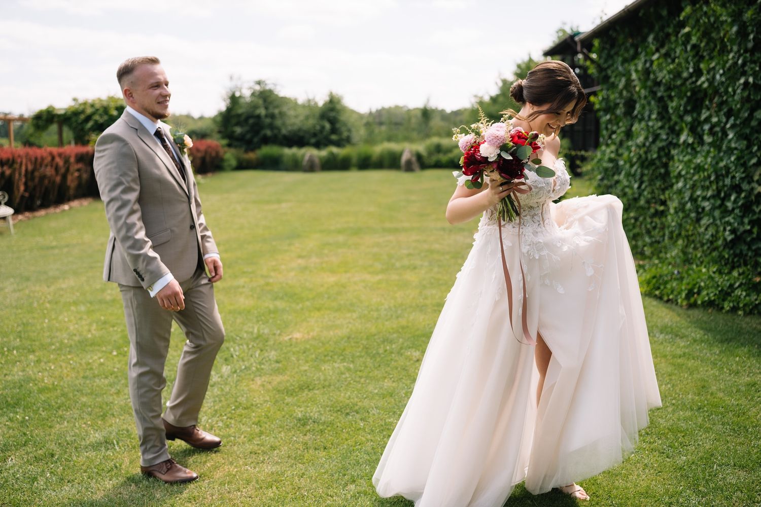 Bride in white gown laughs joyfully with groom during outdoor wedding first look.