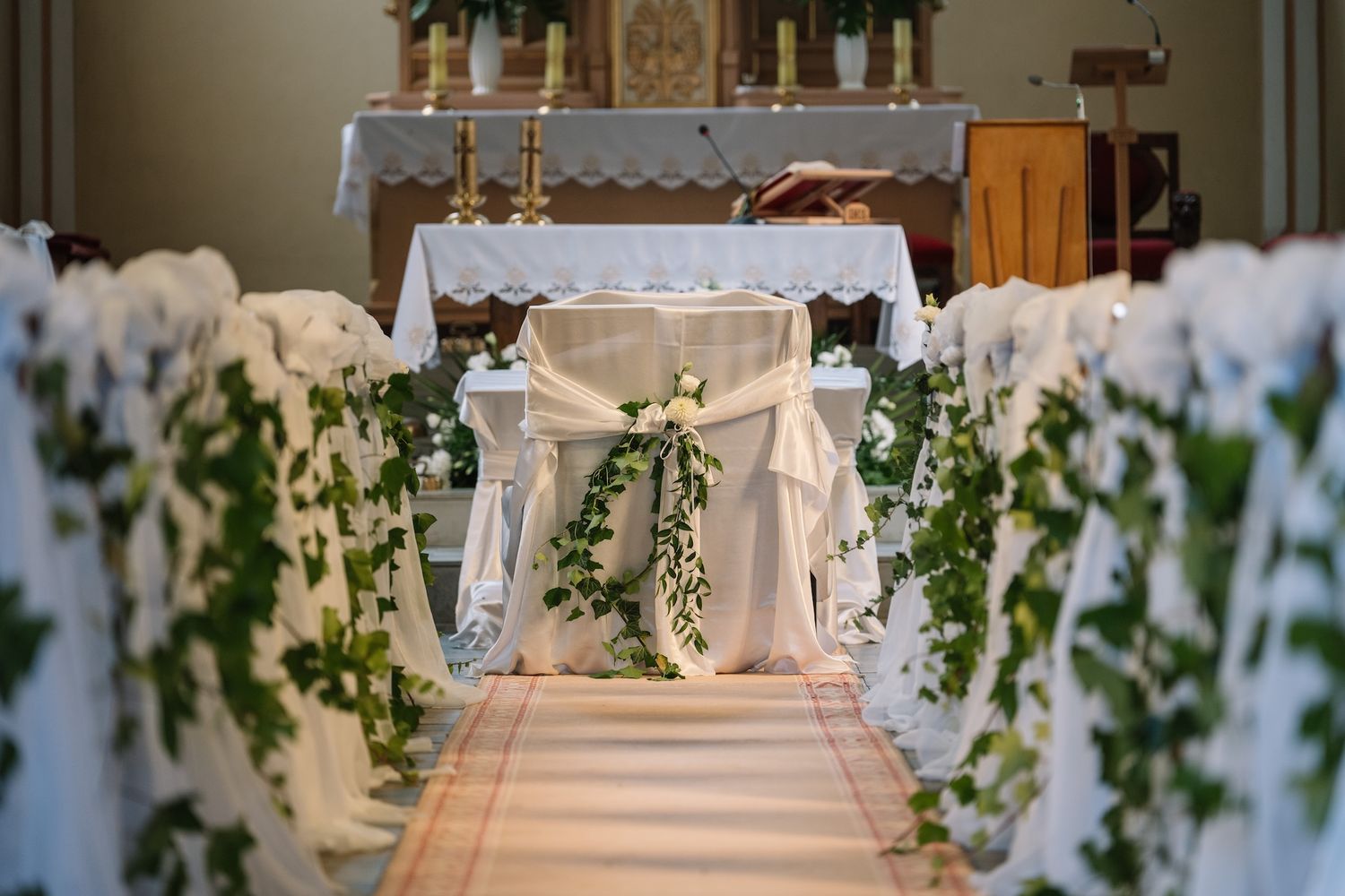 Elegant church aisle decorated with white draping, ivy garlands, and floral arrangements.
