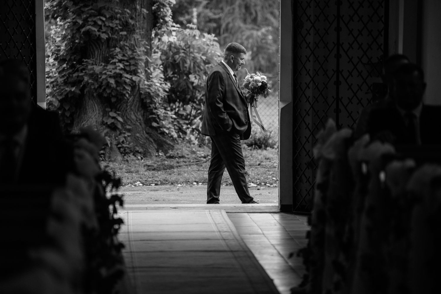 Black and white photo of groom waiting at church entrance before wedding ceremony.