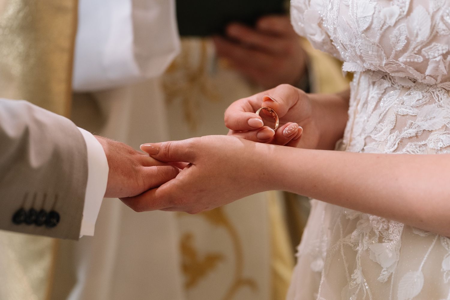 Groom places wedding ring on brides finger during intimate church ceremony exchange of vows.