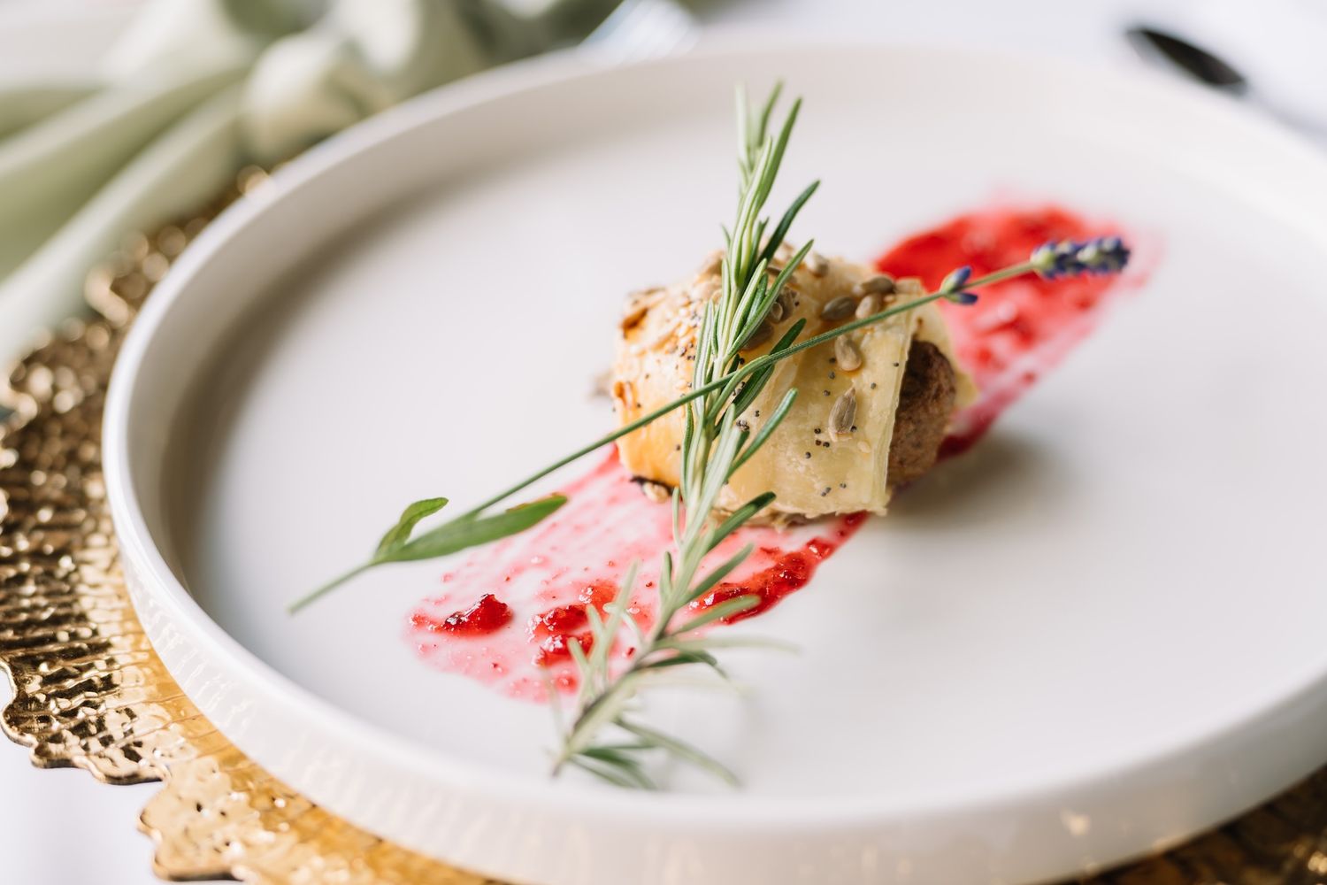 Elegant wedding appetizer with berry sauce and rosemary garnish served on white plate.