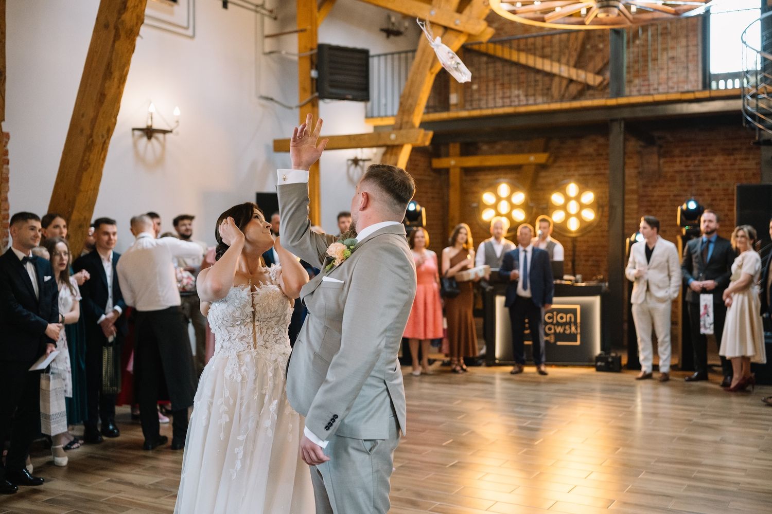 Bride and groom sharing first dance in a rustic brick wedding venue surrounded by celebrating guests.
