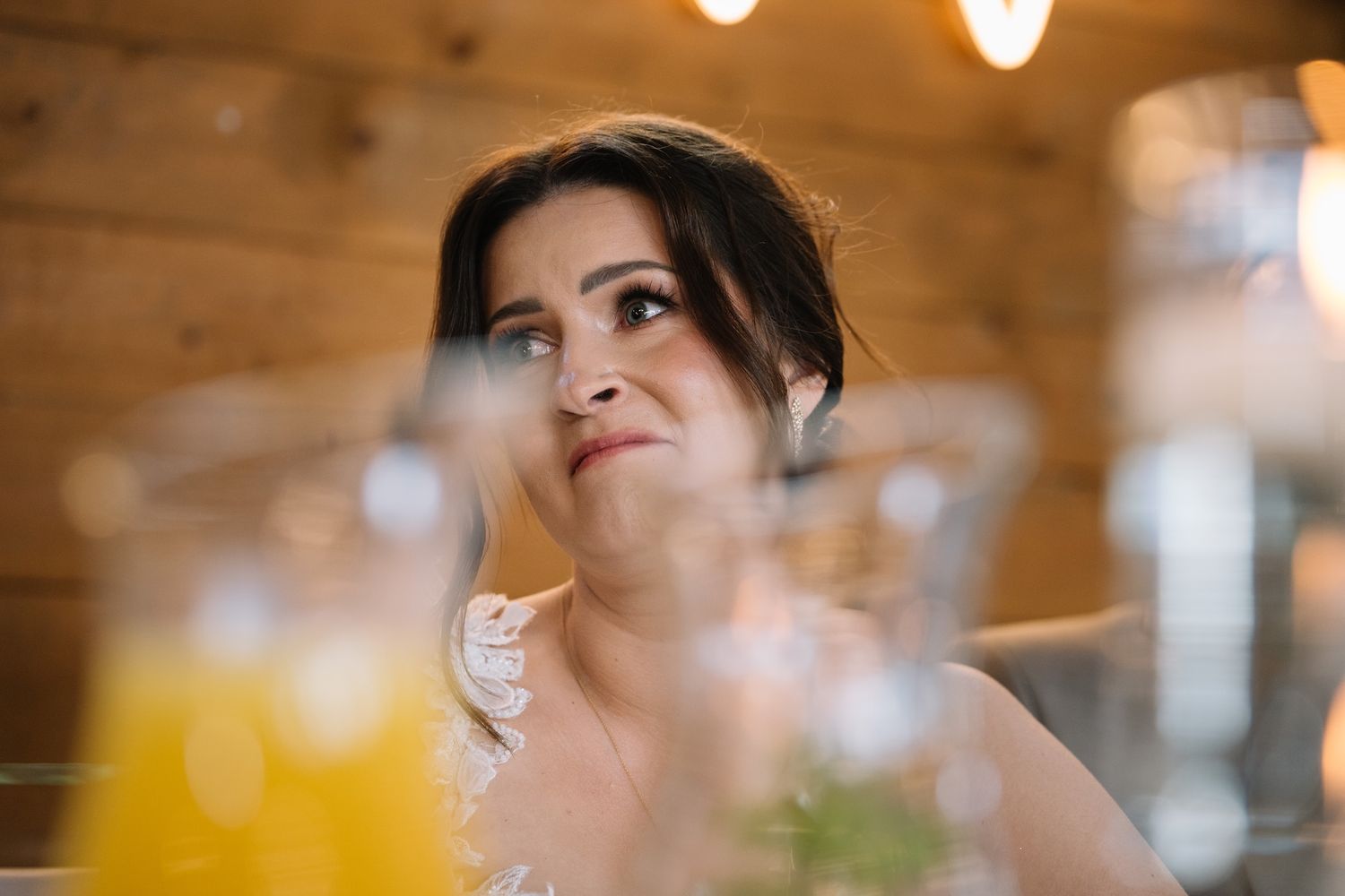 Beautiful bride with updo hairstyle and smoky eye makeup gazing upward at rustic wooden wedding venue.