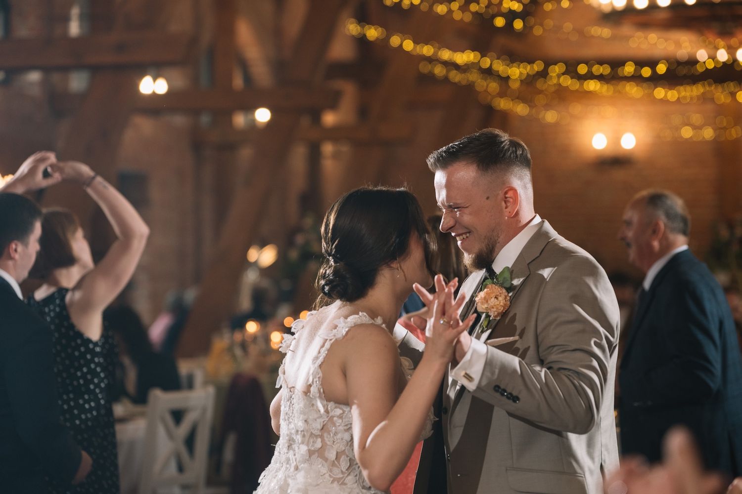 Bride and groom sharing first dance in warmly lit rustic barn venue.