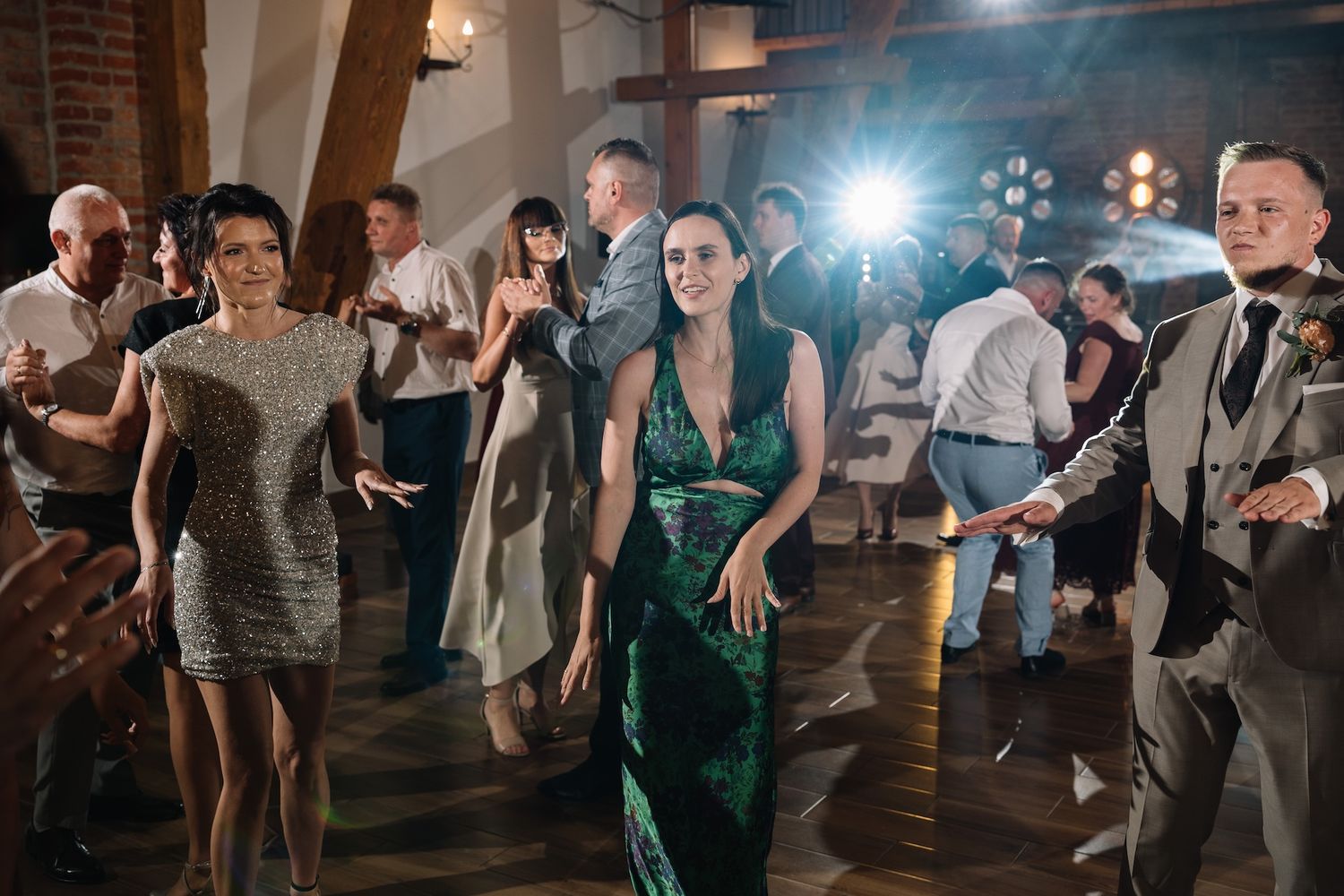 Wedding guests dancing in elegant brick venue with woman in emerald green gown.