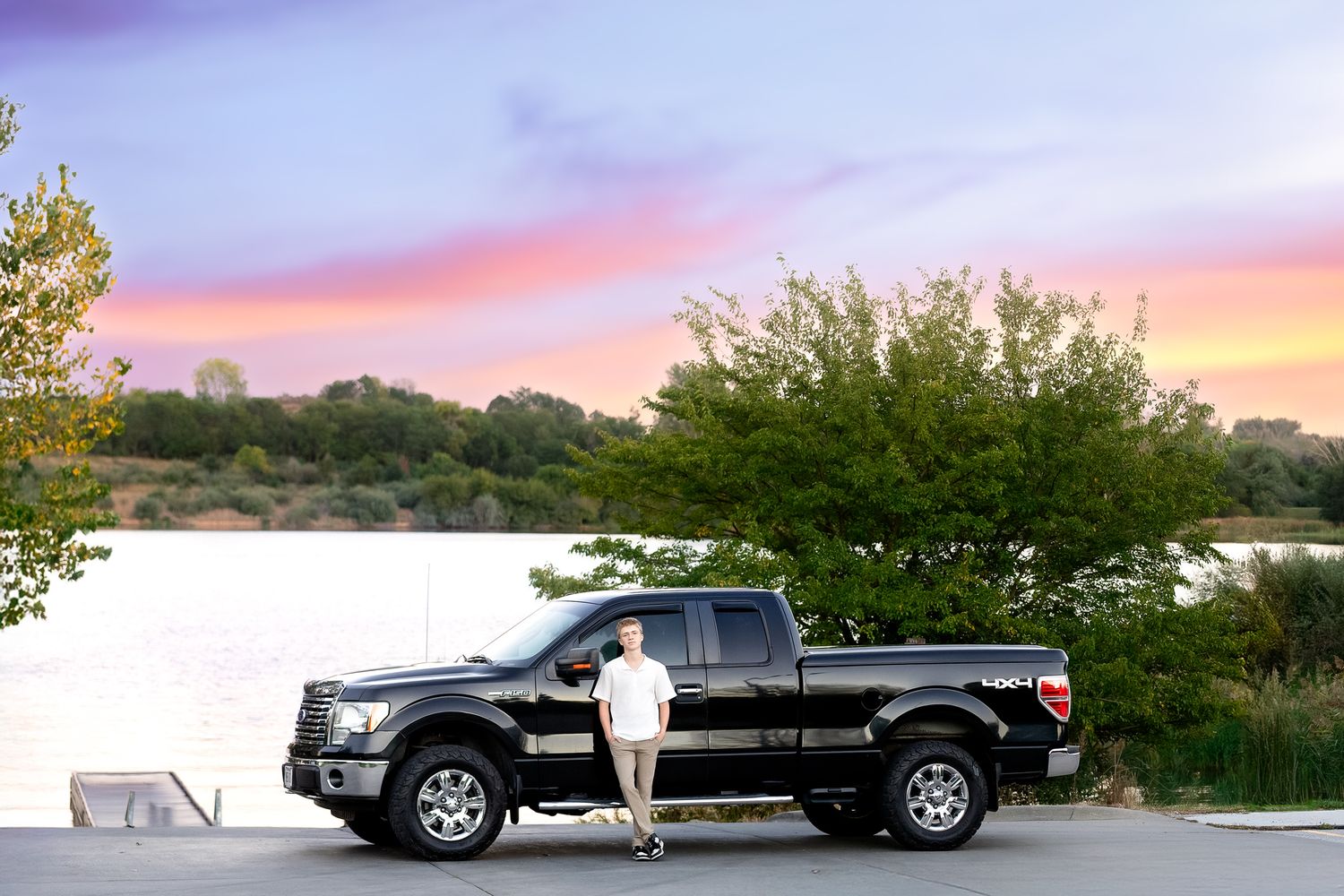 A series of black pickup trucks parked at sunset with colorful sky and trees in the background.