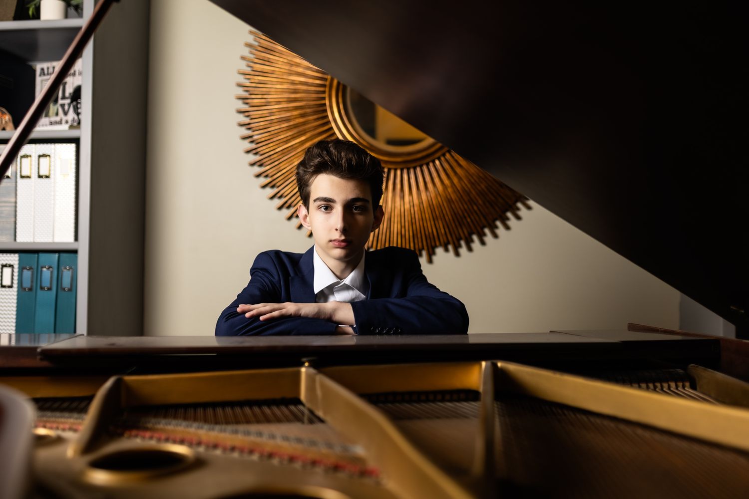 A moody artistic portrait shows someone seated at a grand piano with dramatic lighting and a sunburst decoration on the wall.