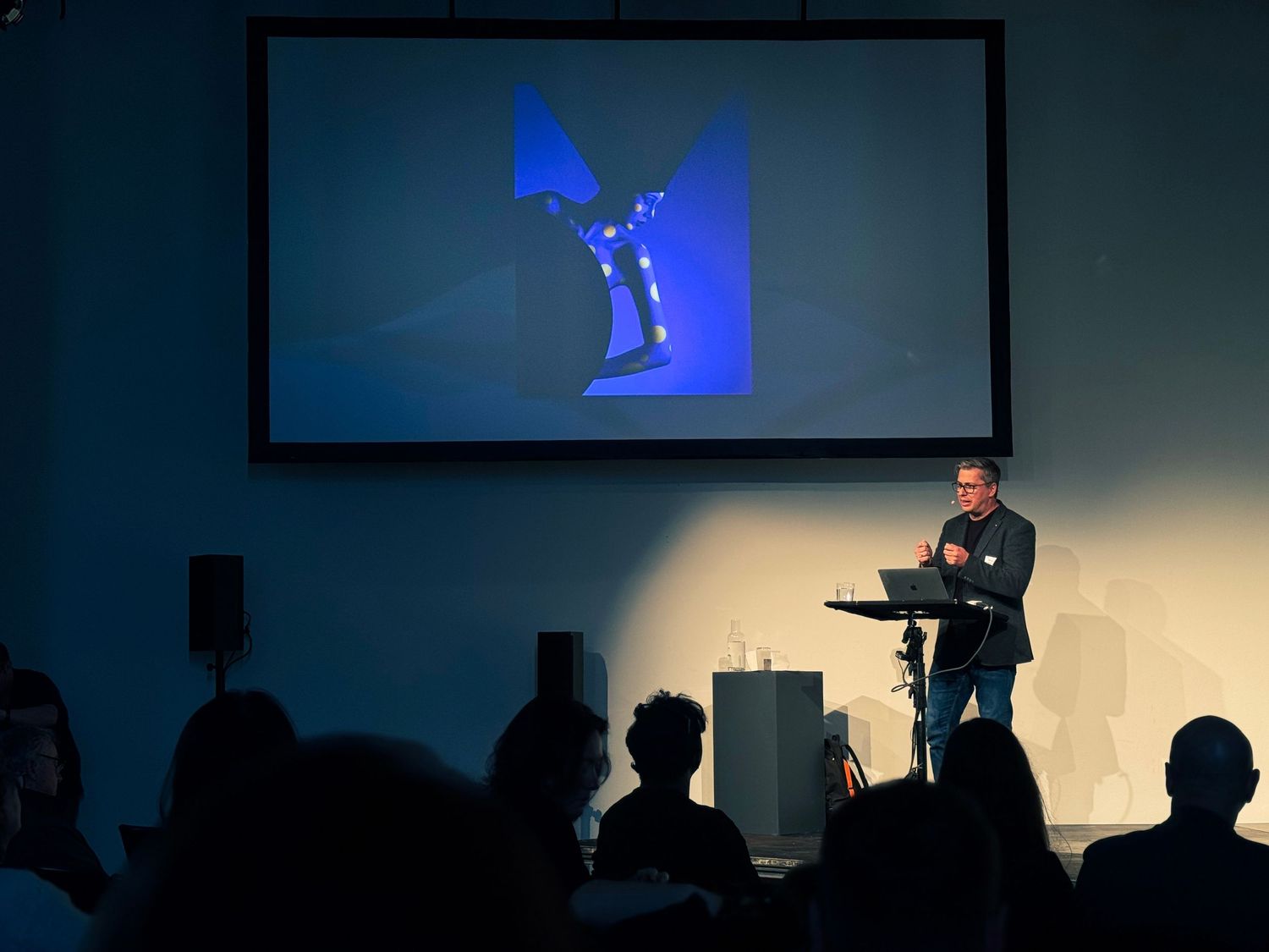 A dark stage with silhouetted figures and blue lighting creates a dramatic performance atmosphere.