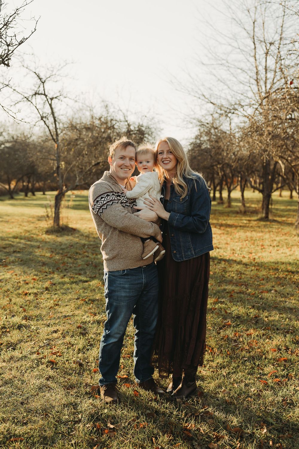 A loving family embraces while standing in a sunlit orchard during golden hour.
