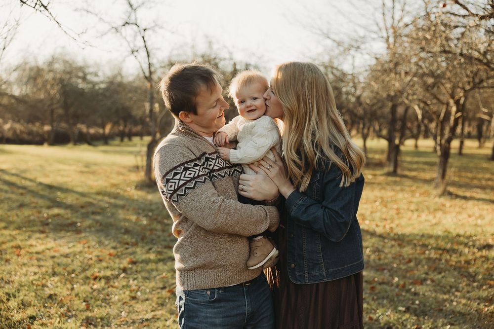 A family shares a tender moment together in an autumn orchard during golden hour.