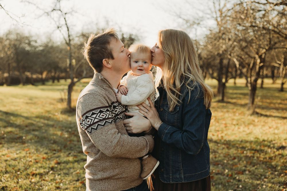 A family shares tender moments together in an autumn orchard during golden hour sunset.