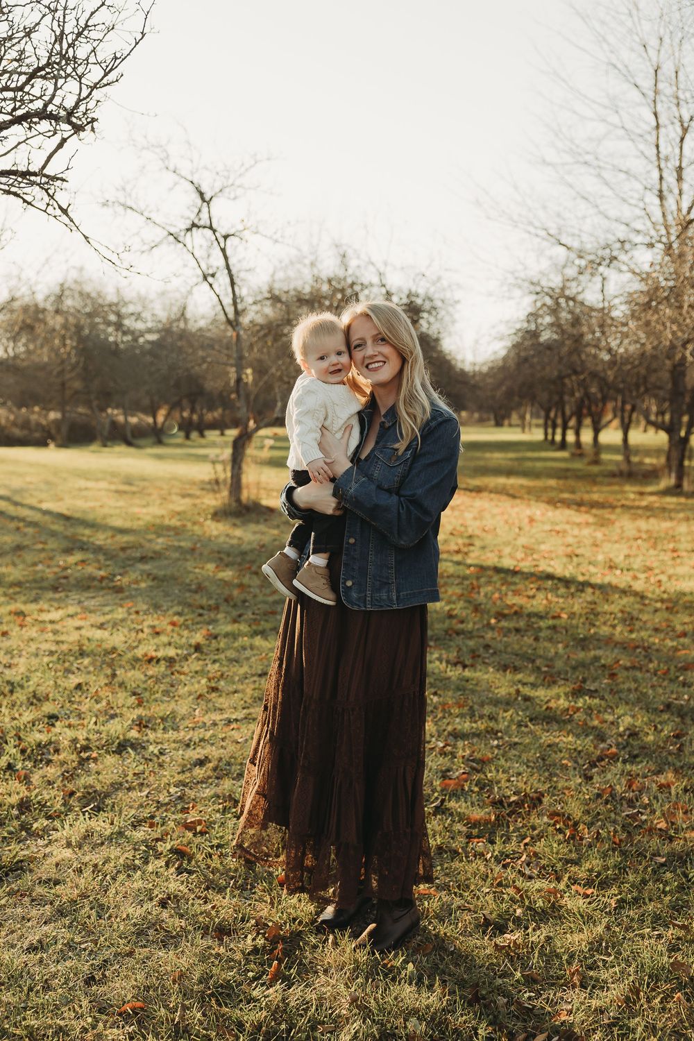 Candid outdoor portraits in a golden field with bare trees at sunset.