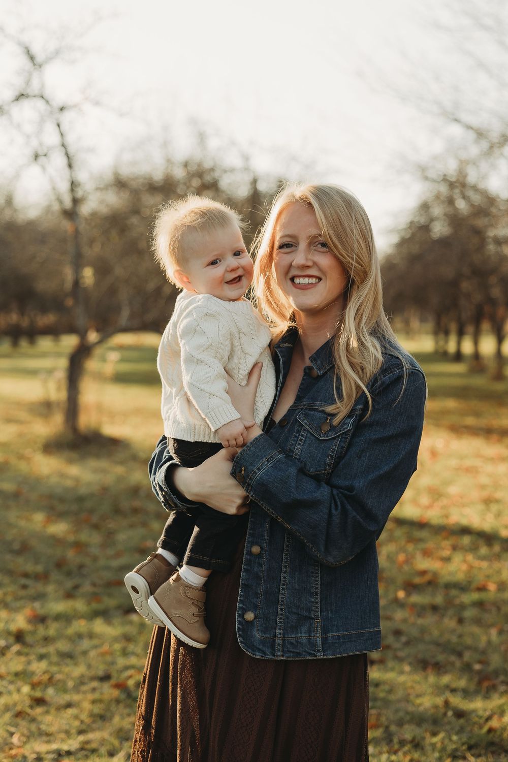 Mother and baby share joyful moments in an autumn orchard during golden hour sunset.