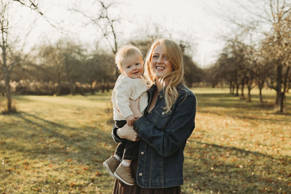 A mother and child share joyful moments together in a sunlit autumn field with golden leaves scattered on the ground.