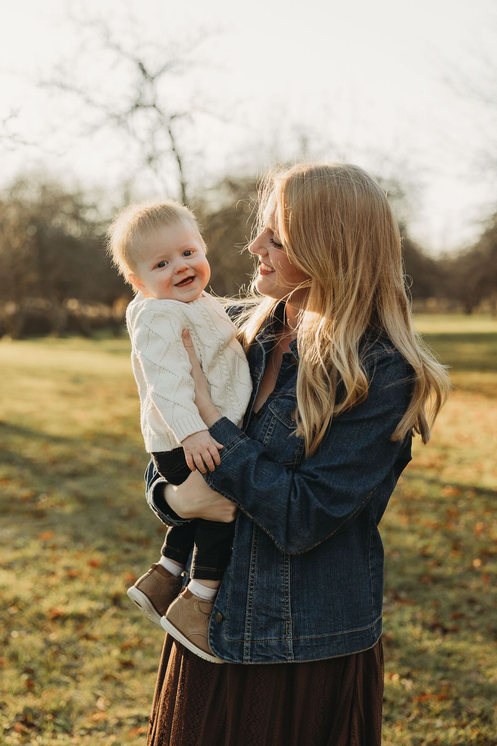 A tender outdoor moment in autumn sunlight shows playful interaction between parent and child in a denim jacket.