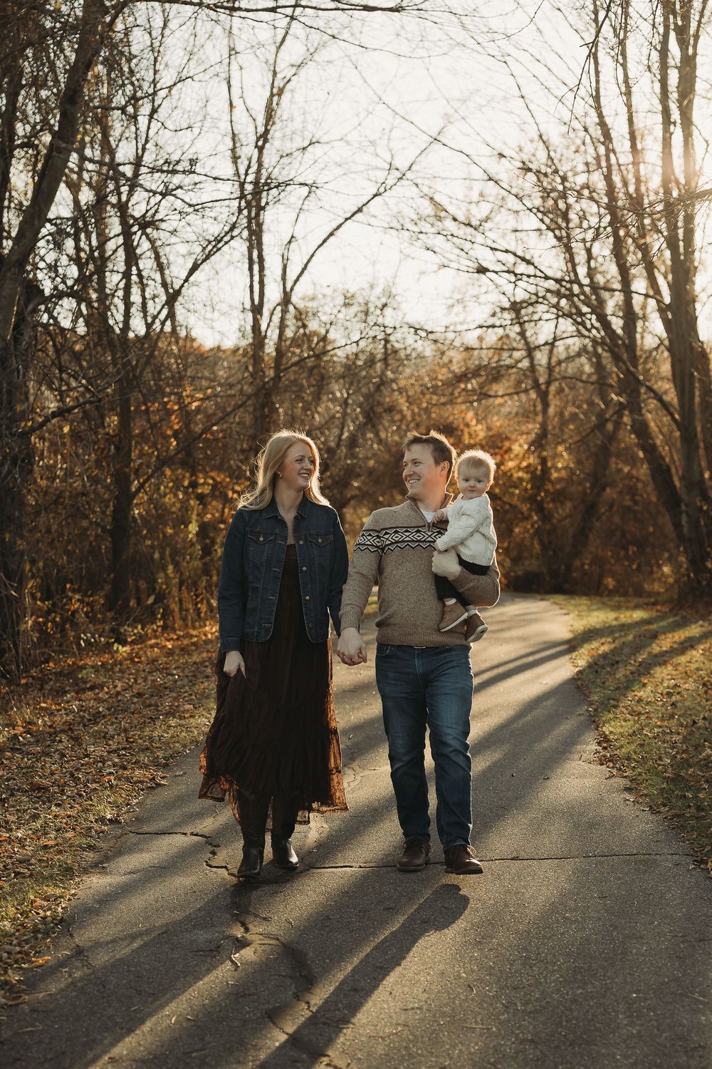 A family takes an autumn stroll together on a sunlit path through bare trees casting long shadows.