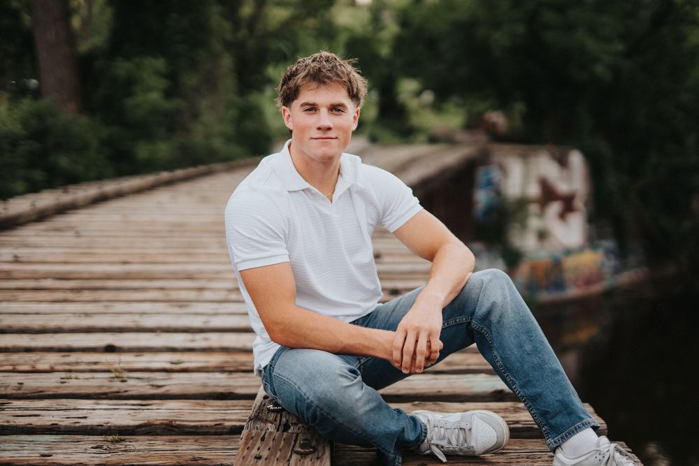 Person in white t-shirt and jeans poses on wooden boardwalk during outdoor photoshoot.