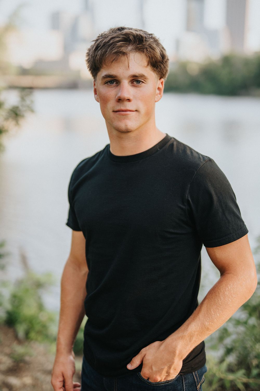Young person wearing a black t-shirt poses outdoors against a blurred natural background.