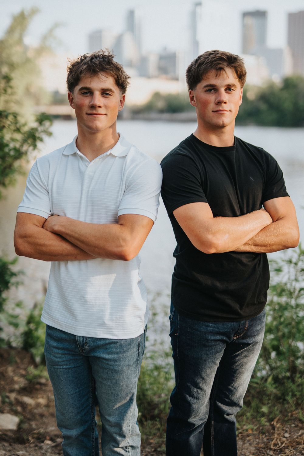 Two people in casual outfits standing together against a city skyline background.