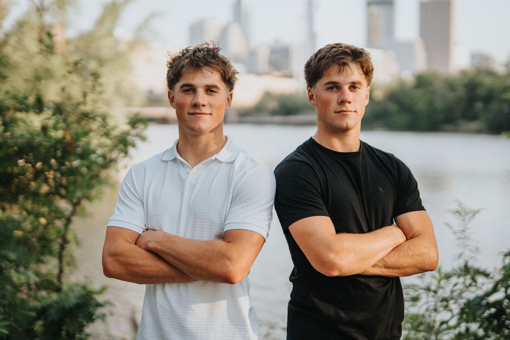 Two people stand side by side wearing contrasting white and black shirts against city backdrop.