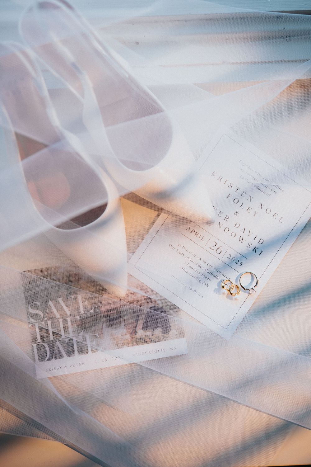 Wedding save the date invitation card with gold rings and white veil in soft dreamy lighting.