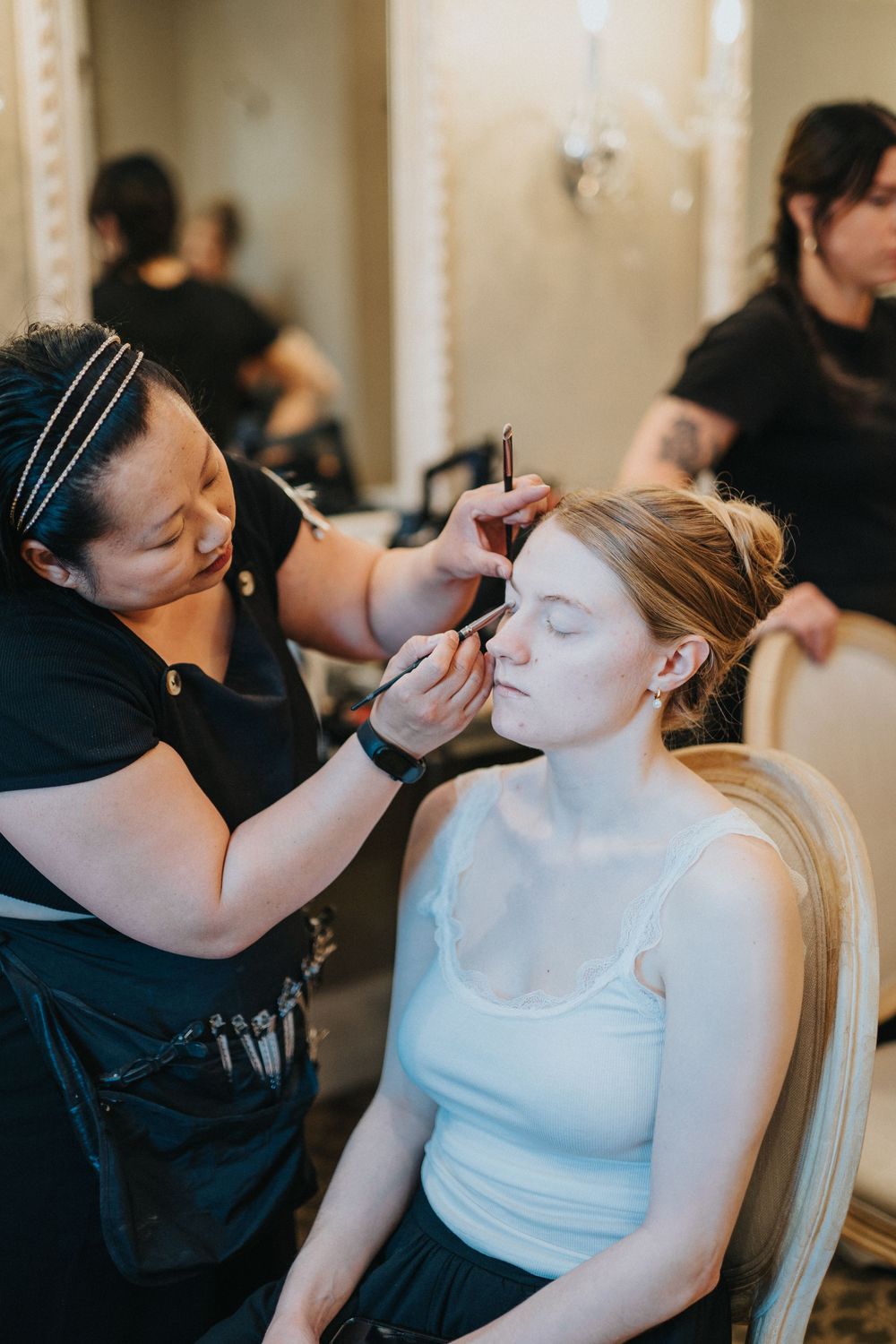 Professional makeup artist applies cosmetics to client's face during preparation session in elegant venue.