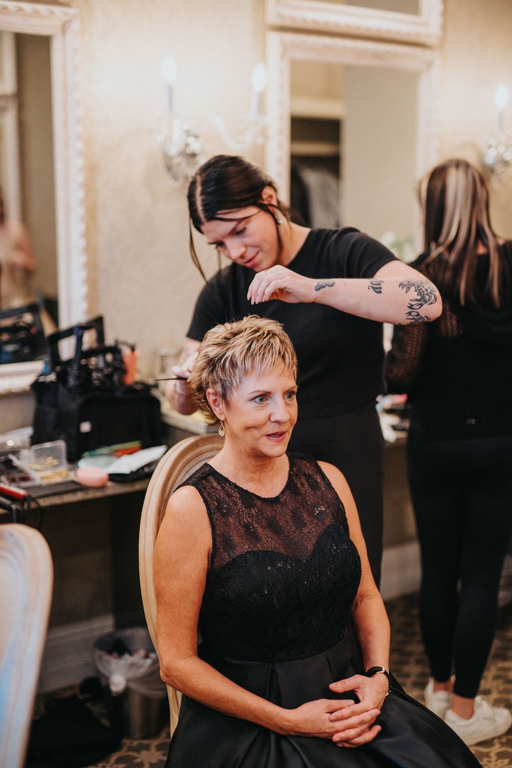 Hair stylist works on a client's short blonde hair in an elegant salon setting.