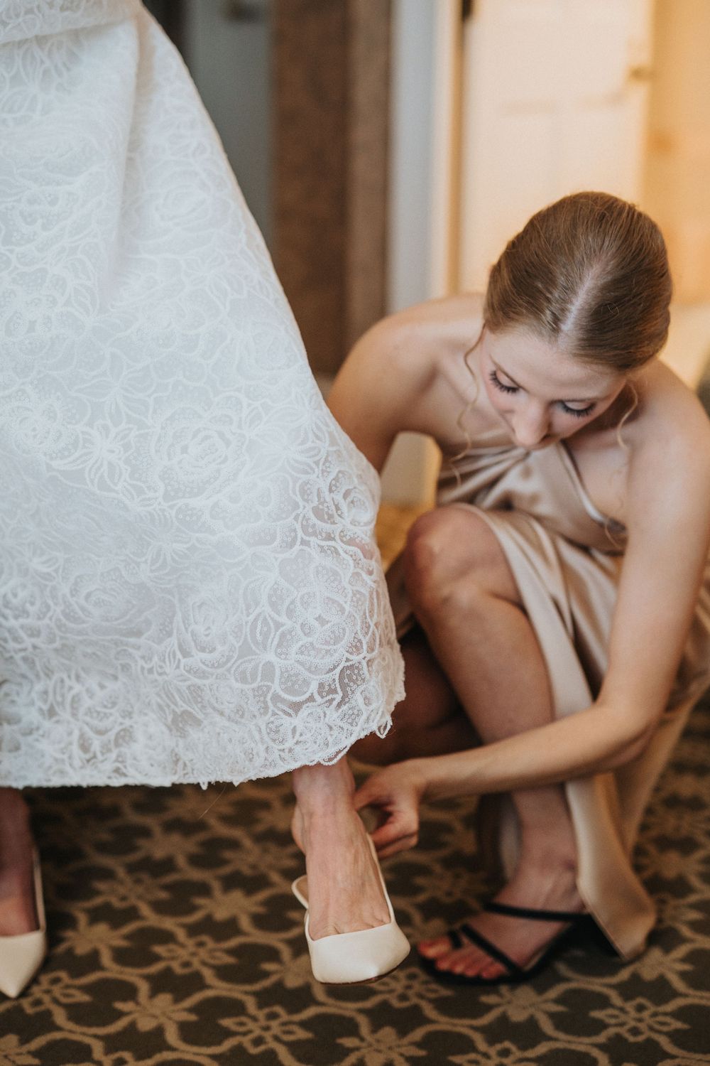 Close-up of someone helping with wedding shoes and accessories on a patterned carpet.