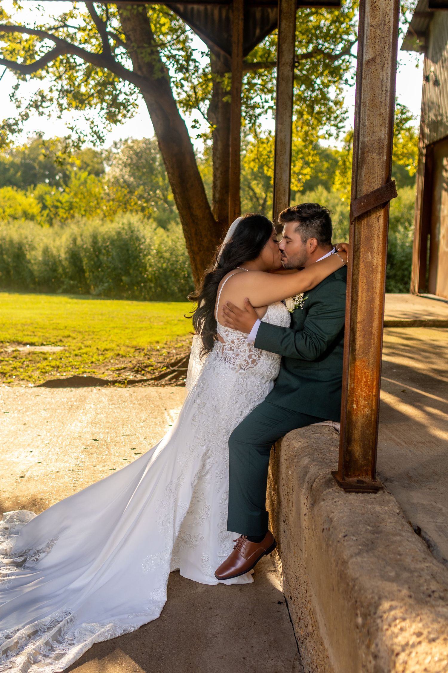 Romantic wedding couple embraces in a rustic wooden pavilion during golden hour sunset.