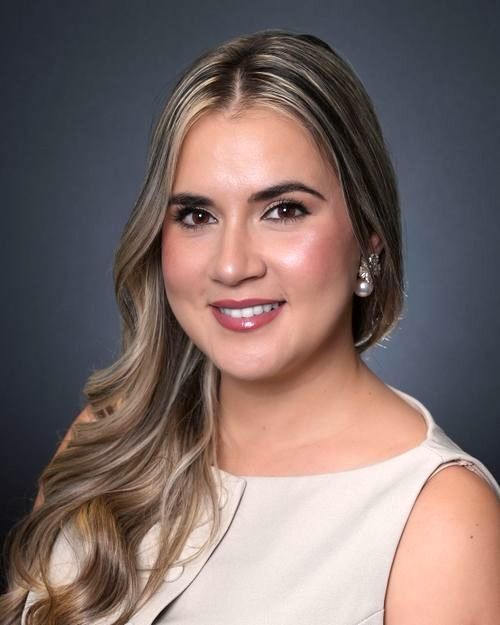 Professional headshot portrait with warm smile wearing a sleeveless white top against dark studio background.