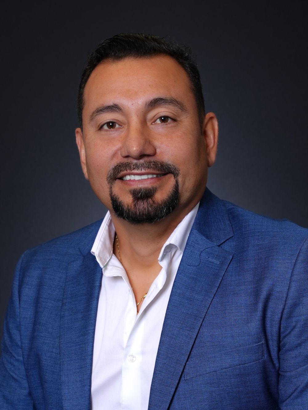Professional headshot of a smiling man in a blue blazer and white shirt against a dark gray background. kw realty headshots