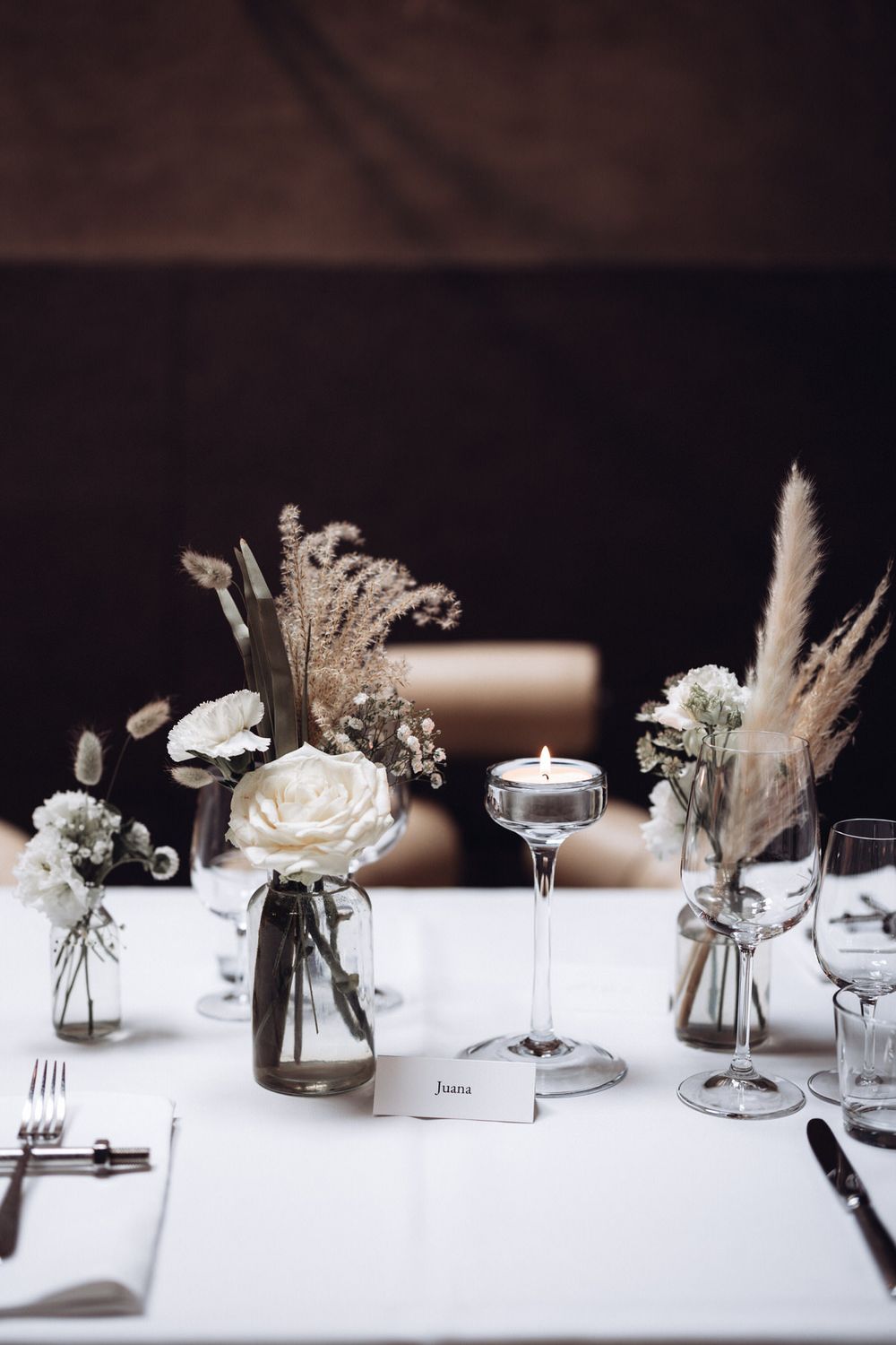 Minimalistische Tischdekoration mit Kerze, Glasvasen und floralen Details – elegante Hochzeitsästhetik in warmem Licht.