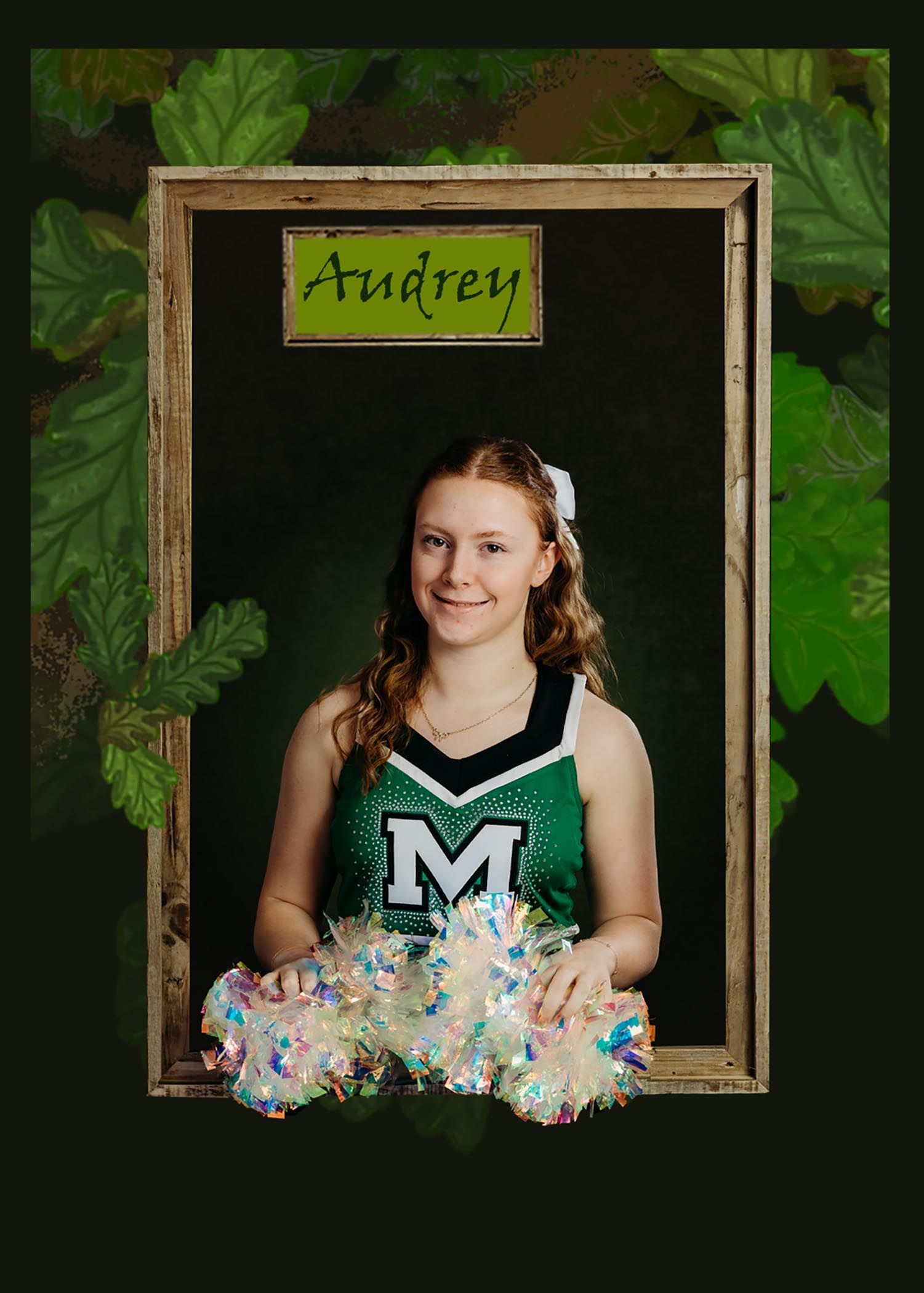 A cheerleader in a green and white uniform with 'M' logo holds pom-poms while posing in a wooden frame against foliage.
