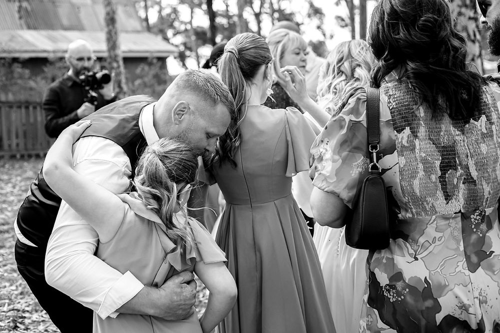 Wedding guests share emotional embraces and greetings during an outdoor celebration.