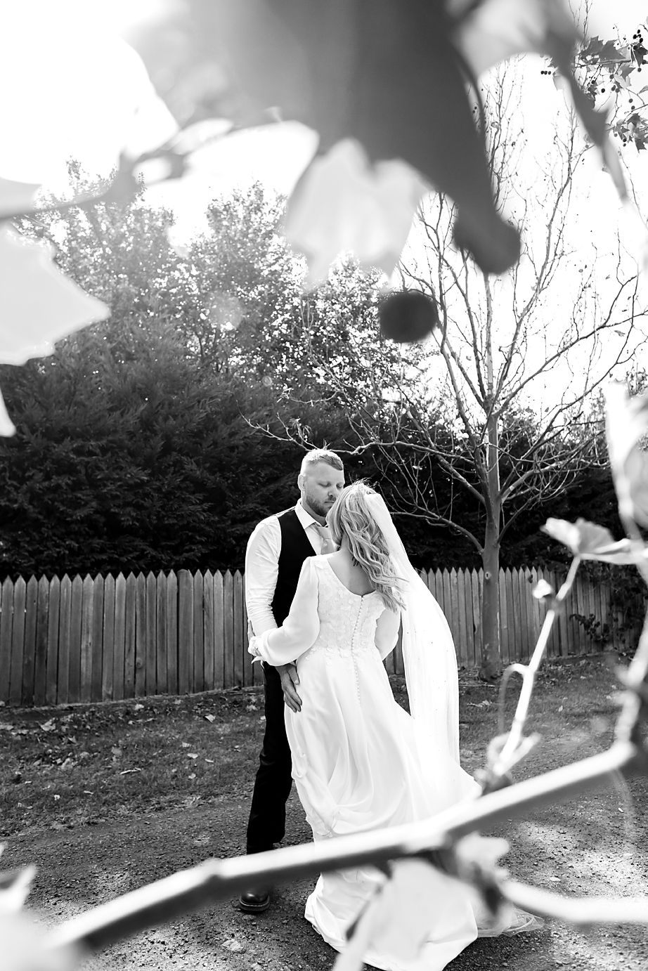 Black and white artistic photo series of a couple dancing outdoors in a backyard with a wooden fence.