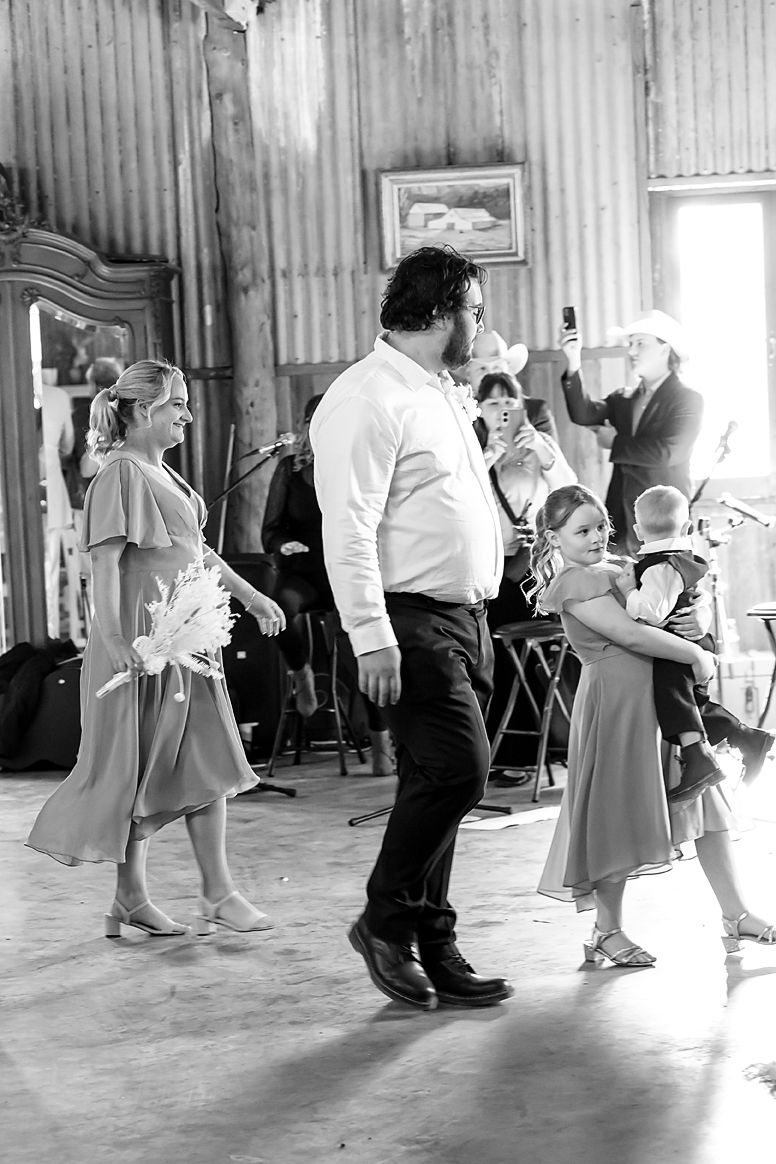 Black and white photo of people dancing at a rustic venue with corrugated metal walls and a wooden dance floor.