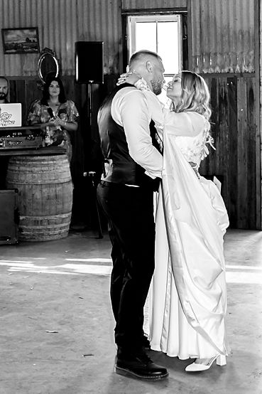 A romantic black and white wedding photo of a couple sharing their first dance in a rustic barn venue.