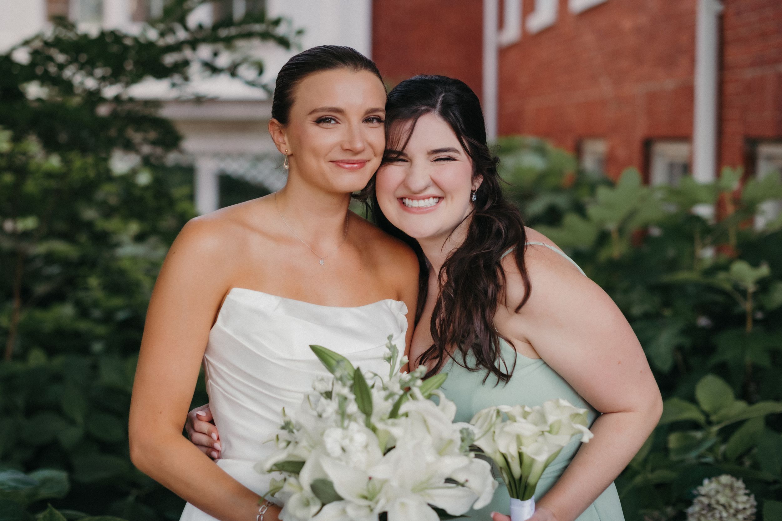 Wedding party members in mint green dresses and white gowns pose together in front of a brick building.
