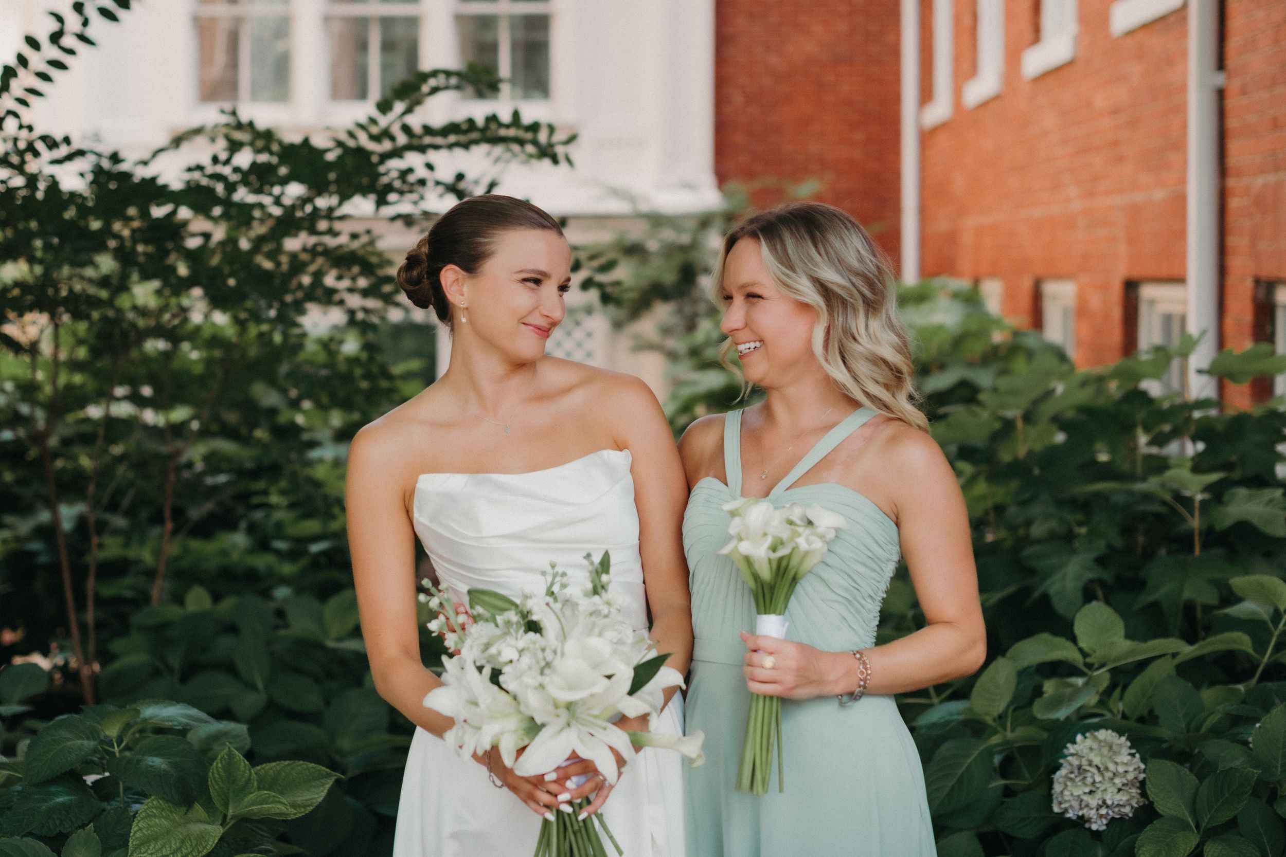 Wedding party in mint bridesmaid dresses and white gowns gather for outdoor photos by brick building.