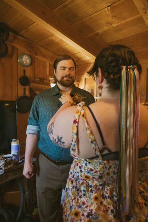 A person wearing a floral apron and blue shirt stands in a rustic wooden cabin interior.