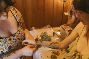 Hands working on wedding preparations with floral arrangements on wooden table.
